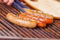 Close up of woman s hand holding a tongs turning the grilling sausages on barbecue grill. BBQ. Bavarian sausages Royalty Free Stock Photo