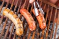 Close up of woman s hand holding a tongs turning the grilling sausages on barbecue grill. BBQ. Bavarian sausages Royalty Free Stock Photo