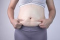 Close-up of woman`s hand pinching excessive belly fat  on gray background. Woman fat belly. Obesity and Overweight Concep Royalty Free Stock Photo