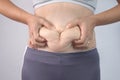 Close-up of woman`s hand pinching excessive belly fat  on gray background. Woman fat belly. Obesity and Overweight Concep Royalty Free Stock Photo