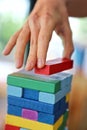 Close-up of woman`s hand pick the red stack on the wooden tower game in morning light , playing and learning background concept