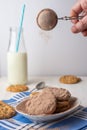Close-up of woman`s hand pouring chocolate powder onto cookies on plate with bottle of milk, with selective focus, on blue napkin Royalty Free Stock Photo