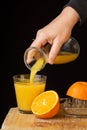 Close-up of woman`s hand serving frozen orange juice with a bottle, over a glass, on wooden table with oranges, black background, Royalty Free Stock Photo