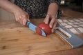 Woman`s hands cutting a tomato into slices with a blue knife on a wooden board at the kitchen counter Royalty Free Stock Photo