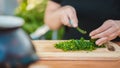 Woman cutting greens on wooden board outdoors. Close up of woman`s hands cutting verdure with knife on chopping board Royalty Free Stock Photo