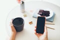 Close-up of woman hands holding cell phone while drinking tea and eating chocolate. Reading news, surfing the web / internet, Royalty Free Stock Photo