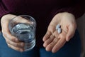 Close-up of woman`s hands holding a glass of water and pills to take. Royalty Free Stock Photo