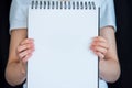 Close-up of woman`s hands holding out a spiral bound notebook with a blank page for copy space