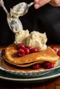 Close-up of woman`s hands with spoons and mascarpone cheese on pancakes with cherries,