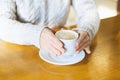 Close-up of a woman`s hands in a warm sweater holding a white Cup of hot coffee, chocolate or tea in a coffee shop against the bac Royalty Free Stock Photo