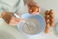 Close up of a woman's hands whipping eggs for making dough on the white desk in the kitchen. Homemade cooking