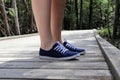 Close-up of a woman's legs in blue sneakers on a boardwalk footpath. Forest in the background. Brokenhead Wetland Trail.