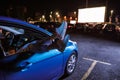 Close up of woman s legs dangling out a car window parked in front of a big white screen at drive in cinema Royalty Free Stock Photo