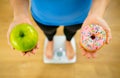 Woman on scale measuring weight holding apple and donuts choosing between healthy or unhealthy food Royalty Free Stock Photo