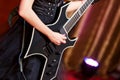 Close-up of a woman on stage playing on electro guitar. The girl rockstar in a black dress