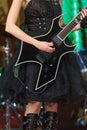 Close-up of a woman on stage playing on electro guitar. The girl rockstar in a black dress