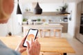 Close Up Of Woman Using App On Smart Phone To Control Central Heating Temperature In House