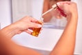 Close Up Of Woman Using Beauty Serum From Bottle In Bathroom At Home Wearing Towel