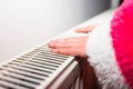 Close-up of a woman warming up her hands on a white radiator at home. Central heating concept Royalty Free Stock Photo