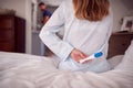 Close Up Of Woman Wearing Pyjamas Holding Positive Pregnancy Test Behind Back In Bedroom