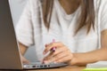 Close up of a woman wearing a white shirt and holding the pen and placing her hand near the grey laptop computer keyboard Wooden Royalty Free Stock Photo