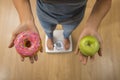 Close up woman on weight scale holding in her hand apple fruit and donut as choice of healthy versus unhealthy food Royalty Free Stock Photo