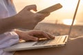 Close up of woman working with laptop and mobile phone on the beach by the sea during sunset. Female freelancer work Royalty Free Stock Photo