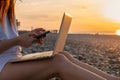 Close up of woman working with laptop and mobile phone on the beach by the sea during sunset. Female freelancer work Royalty Free Stock Photo