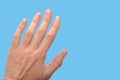 Close-up of a woman& x27;s age-old hand with wrinkles with natural nails, overgrown cuticle on blue background
