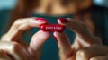 Close-up of a woman& x27;s fingers holding a red painkiller capsule with a manicured hand.