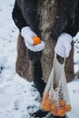 Close up of woman& x27;s hands holding a bag with mandarines, outdoors in the forest with snow Royalty Free Stock Photo