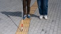 Close-up of a woman's legs accompanying a blind elderly lady outdoors.