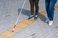 Close-up of a woman's legs accompanying a blind elderly lady outdoors.