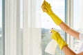 Close up of woman in yellow rubber gloves cleaning window with cleanser spray and yellow rag at home or office, copy space.