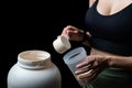 Close up of women with measuring scoop of whey protein, jar and shaker bottle, preparing protein shake