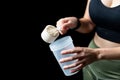 Close up of women with measuring scoop of whey protein and shaker bottle, preparing protein shake