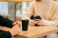 Close-up of woman and man sitting in cafe holding warm cups of coffee on table having fun conversation. Royalty Free Stock Photo