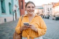 Woman wearing orange yellow shirt texting on the smart phone walking in the street in a sunny day Royalty Free Stock Photo