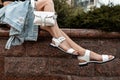 Close-up of womens legs in stylish leather summer shoes with a white stylish handbag on street