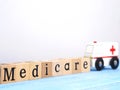 Close up wooden blocks wording Medicare and small white ambulance model on blue wood background