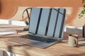 Close up of wooden designer desktop with reflections on laptop screen, coffee cup, supplies and other items.