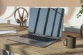 Close up of wooden designer workspace with reflections on laptop screen, coffee cup, supplies and other items.