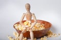 Close up of figurine holding popcorn in arms sitting on the edge of movie theater popcorn bowl on solid background