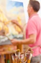 Close up of wooden flask with paint brushes, with blurred man painting as background