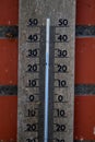 A close up of a wooden mercury thermometer indicating the outdoor temperature in degrees celcius and is hanging on a red brick