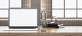 Close up of wooden office desk with empty white computer, supplies and other objects. Blurry brick wall and window with city view Royalty Free Stock Photo