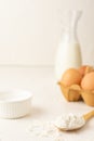 Close-up of wooden spoon with flour, milk bottle and carton with eggs, on white table, selective focus, white background,