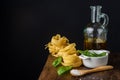 Close-up of wooden spoon with salt, basil in bowl, bottle with olive oil and raw tagliatelle, on wooden table, black background