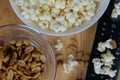 Close-up of a wooden table featuring a bowl of popcorn, a bowl of nuts, and a remote control