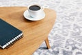 Close-up of a wooden table with a spiral notepad and a cup of coffee with a blurry background of a patterned rug. Real photo.